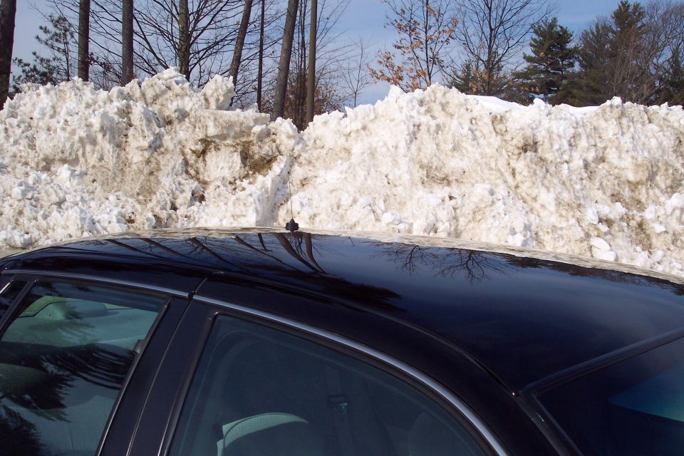 Black sedan roof and side window with a large snowbank behind it