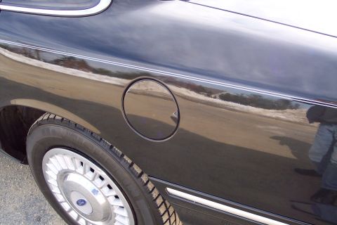 2001 Ford Crown Victoria - Close-up of a black car's rear quarter panel, a circular fuel door and a wheel.