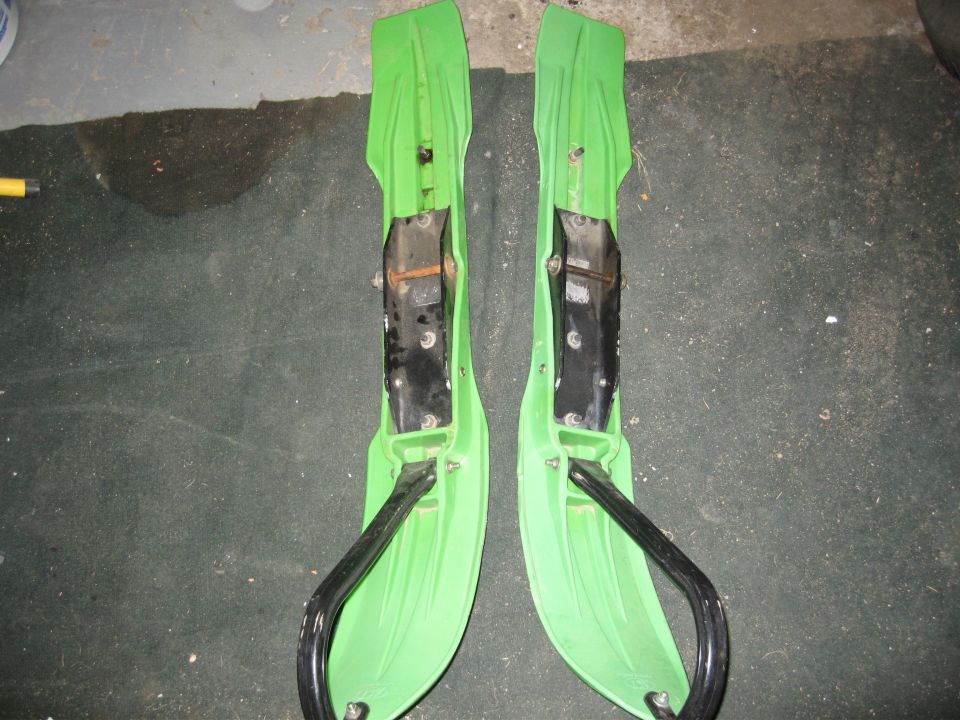 Two green snowmobile skis with black metal ski loops and black plastic runners