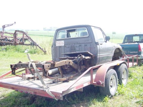 1992 Ford Bronco - A disassembled truck chassis is loaded onto a trailer, with another pickup truck visible in the background.