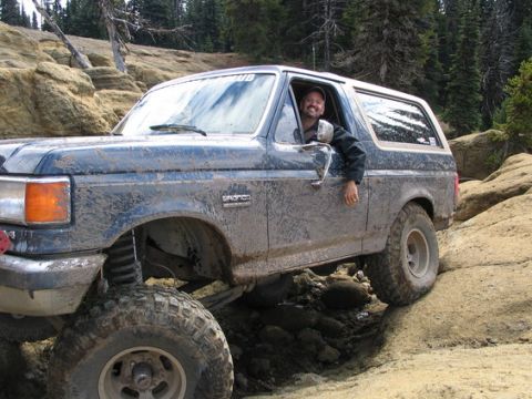 1991 Ford Bronco - A man drives a muddy Ford Bronco through a challenging off-road course.