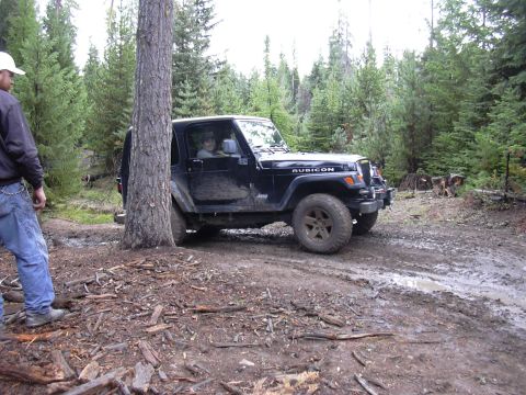 1991 Ford Bronco - A black Jeep Wrangler Rubicon is parked on a muddy trail surrounded by trees. A person wearing a white hard hat and blue jeans stands to th…