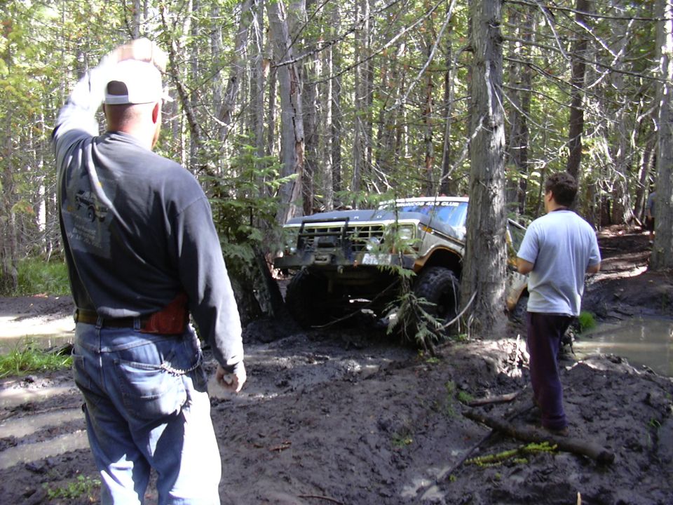 1991 Ford Bronco stuck in mud in a forest, with two men standing nearby.