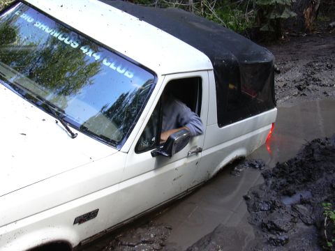 1991 Ford Bronco - A white 1991 Ford Bronco navigates a muddy off-road trail, its tires deep in the mire.
