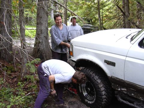 1991 Ford Bronco - Two men are working on a white Ford Bronco that is stuck in the mud in a wooded area. The Bronco has large off-road tires and mud splattere…