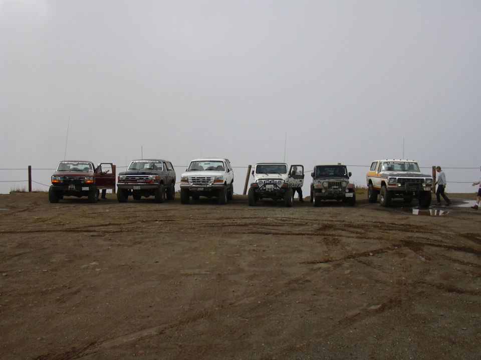 Seven off-road vehicles parked on a dirt lot.