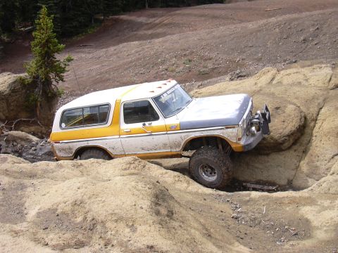 1991 Ford Bronco - A two-tone yellow and white off-road vehicle navigates a rocky, dirt terrain with its front tire raised.