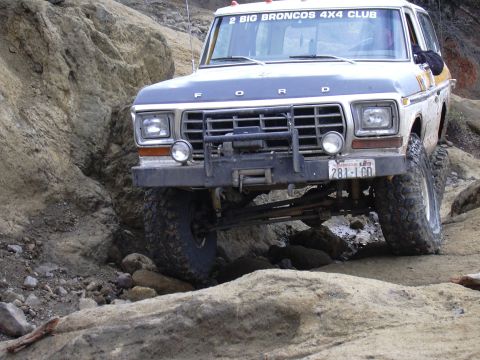 1991 Ford Bronco - A dark blue and white Ford Bronco is navigating a rocky, off-road terrain. The vehicle has a winch mounted on the front bumper and a sticke…