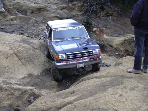 1991 Ford Bronco - A blue 1991 Ford Bronco is navigating a rocky, off-road trail. The vehicle has "2 BIG BRONCOS 4x4 CLUB" text on the windshield and a licens…