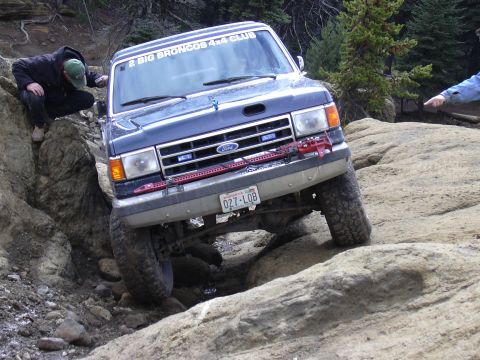 1991 Ford Bronco - An SUV navigates a steep, muddy incline during an off-road event.