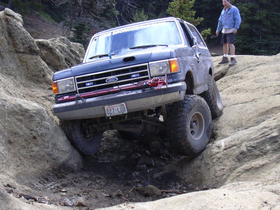 Ford Bronco climbing over rocks on a trail. License plate reads 027-LOB