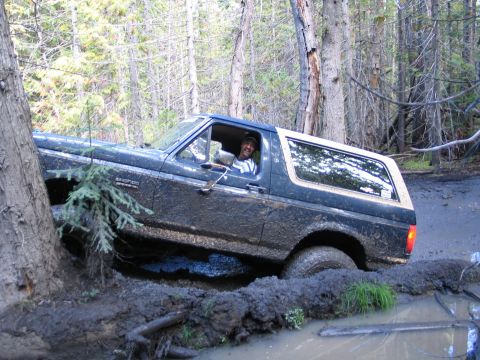1991 Ford Bronco - A driver smiles from inside a heavily mud-caked 1992 Ford Bronco navigating a difficult off-road path.