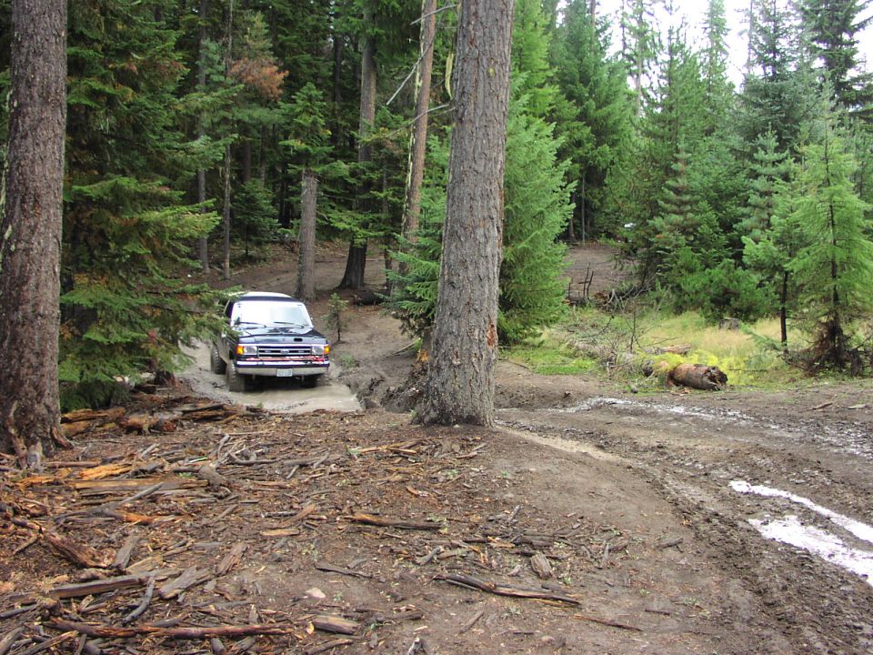 Black 1991 Ford Bronco driving on a muddy forest trail