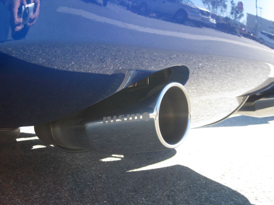 Polished Nismo-branded exhaust tip under the rear bumper of a dark car, shot from ground level