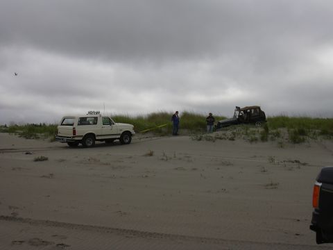 1991 Ford Bronco - A white 1991 Ford Bronco is seen towing a stuck vehicle out of the sand dunes on an overcast day.