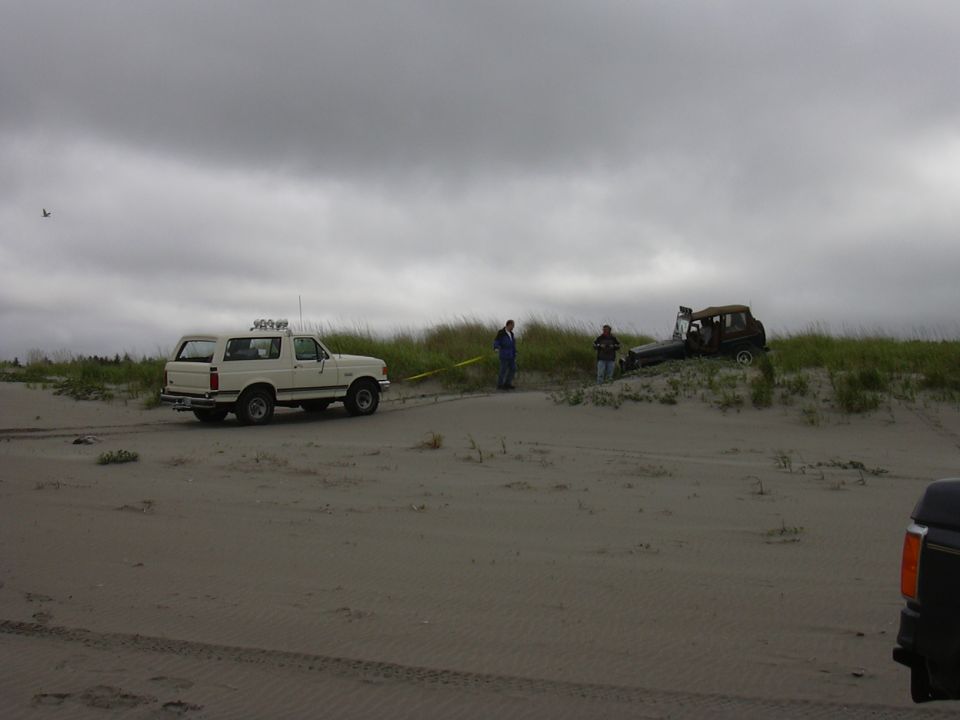 White 1991 Ford Bronco towing a stuck vehicle on a sandy dune