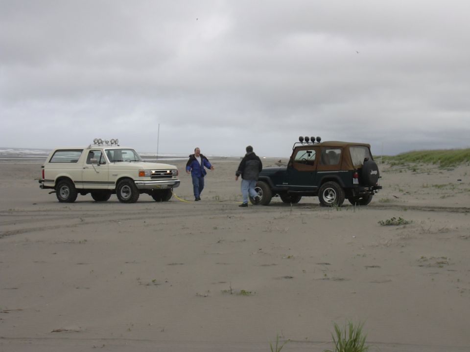 1991 Ford Bronco and a Jeep Wrangler on a beach with two people nearby
