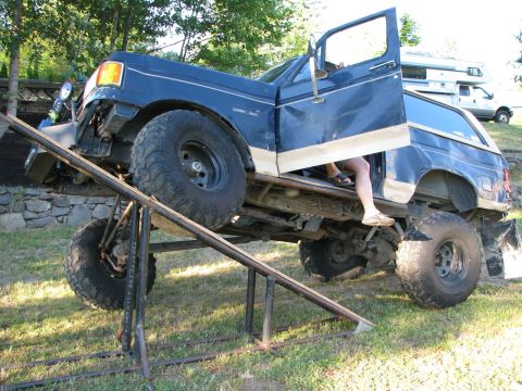 1991 Ford Bronco - A modified blue Ford Bronco is positioned on a metal ramp, with its driver's door open and a person visible inside.