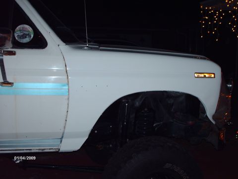 1982 Ford F-100 - Close-up of a white pickup truck's side, showing the front fender and part of the door with a blue stripe.