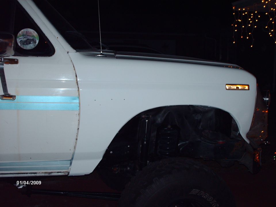 White lifted Ford pickup fender at night with trimmed wheel opening and Pro Comp mud tire