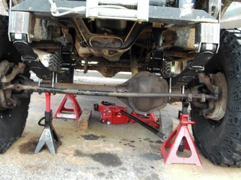1990 Ford Bronco - The underside of a heavily modified 4x4 vehicle is supported by jack stands, revealing its robust suspension components.