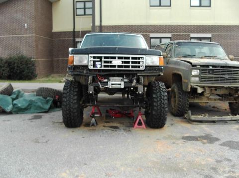 1990 Ford Bronco - A 1990 Ford Bronco is shown on jack stands with a winch installed, parked next to another truck.