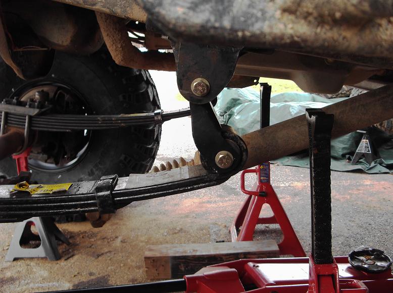 Underneath view of vehicle suspension with leaf springs and shock absorber mount, supported by jack stands