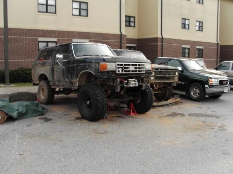 1990 Ford Bronco - A lifted Ford Bronco is parked outside a building with other vehicles, appearing to be undergoing modifications.