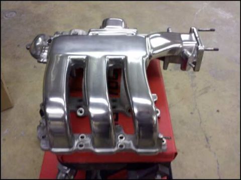 1994 Ford Probe - A shiny intake manifold is shown from a three-quarter front angle, resting on a red surface.