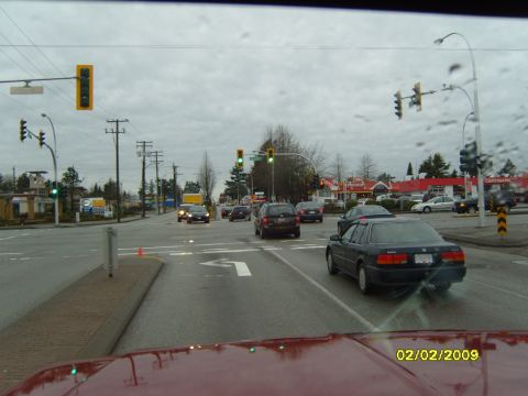 1989 Ford Bronco - View from inside a red vehicle at a busy intersection with multiple cars and traffic lights under a cloudy sky.