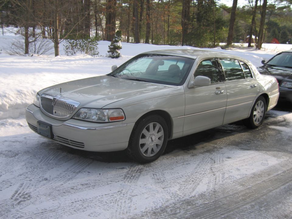 Light-colored Lincoln Town Car parked on a snowy driveway, with another dark vehicle partially visible behind it