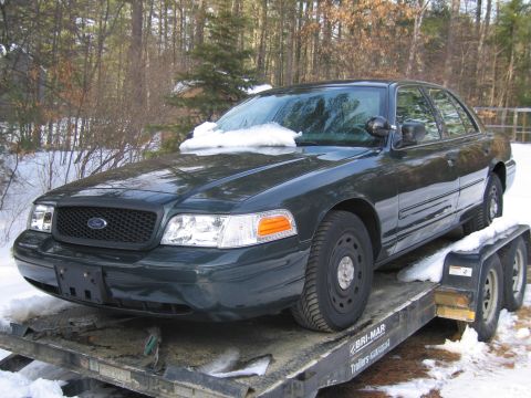 1991 Ford Crown Victoria LTD - A dark green sedan is loaded onto a trailer in a snowy environment, with trees in the background.