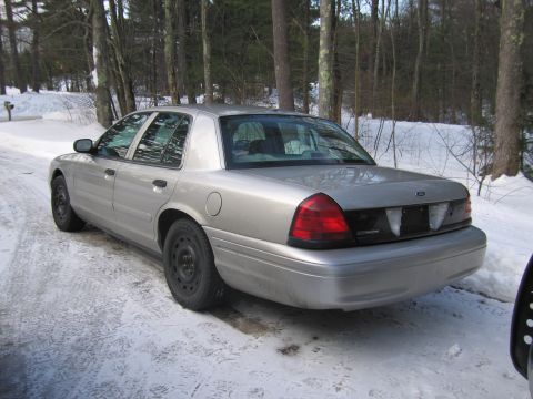 1991 Ford LTD Crown Victoria - A silver Ford Crown Victoria is parked on a snow-covered road, surrounded by trees.