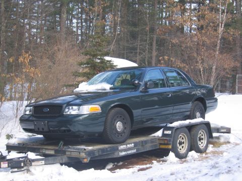 1991 Ford LTD Crown Victoria - A dark green sedan is parked on a trailer in a snowy environment, with trees in the background.