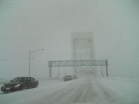 2000 Chevrolet Tahoe - A dark sedan navigates a snow-covered highway, approaching a large bridge structure during a winter storm.