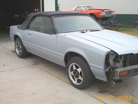1984 Ford Mustang - Primer gray 1984 Ford Mustang convertible with a black top is parked outside a garage.