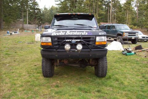 1995 Ford Bronco - Front view of a 1995 Ford Bronco modified for off-road use, parked in a grassy yard with other vehicles.