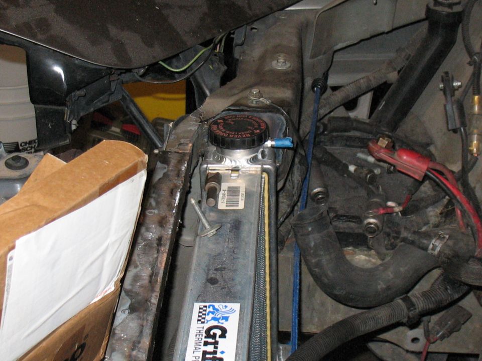 Car engine bay showing radiator, hoses, and wiring. Some parts are covered by a cardboard box