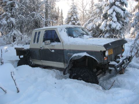 1990 Ford F-250 - A 1990 Ford F-250 is stuck deep in the snow, showing its front 3/4 view with a two-tone paint scheme.