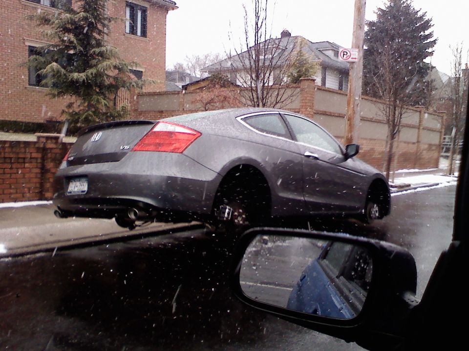 Gray Honda Accord coupe on street, missing all four wheels, snow falling