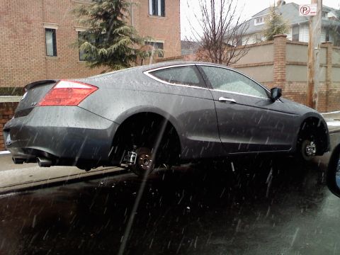 2007 Subaru Impreza - A car sits on blocks with its wheels removed, in the rain.