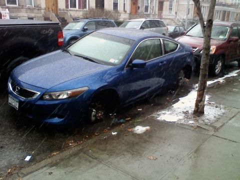 2007 Subaru Impreza - A blue coupe is parked on a wet street during a snowfall, with one of its front wheels missing.