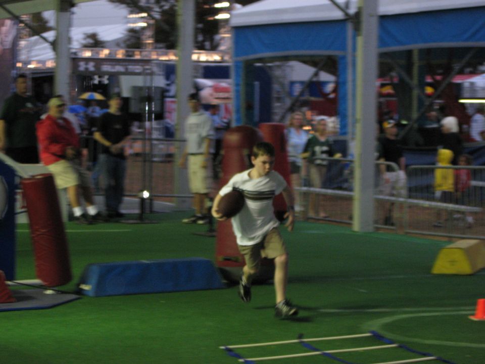 Boy in striped shirt runs with a football on a green turf field with people in the background