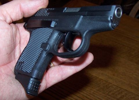 1990 Ford Bronco - A black semi-automatic pistol is held in a person's hand against a wooden background.