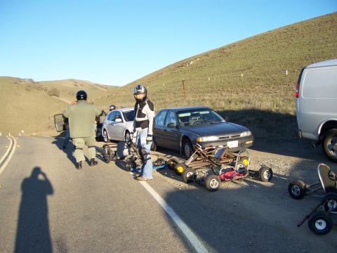 1991 Ford Bronco - Several go-karts and cars are parked on the side of a road with people present.