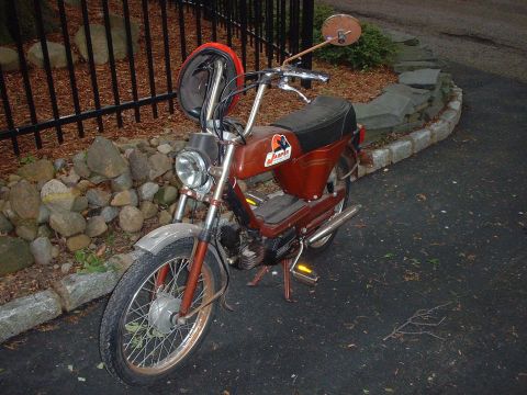 1981 Garelli Rally Sport - A brown moped is parked on an asphalt surface, with a helmet hanging from its handlebars. The side of the moped displays the text 'JAPAR'.