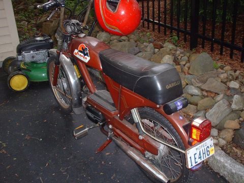 1981 Garelli Rally Sport - A red helmet hangs from the handlebars of a brown moped parked next to a lawnmower.