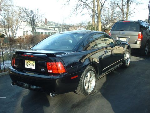 2002 Ford Mustang - This black 2002 Ford Mustang GT is parked in a driveway next to a gray SUV.