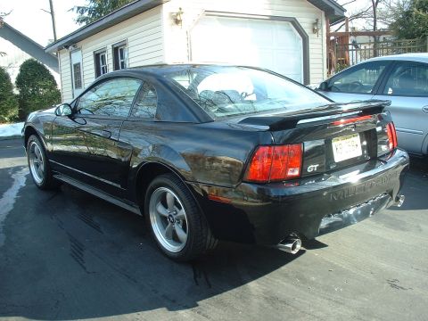 2002 Ford Mustang - Rear view of a black 2002 Ford Mustang GT coupe parked in front of a garage, with another vehicle to its side.