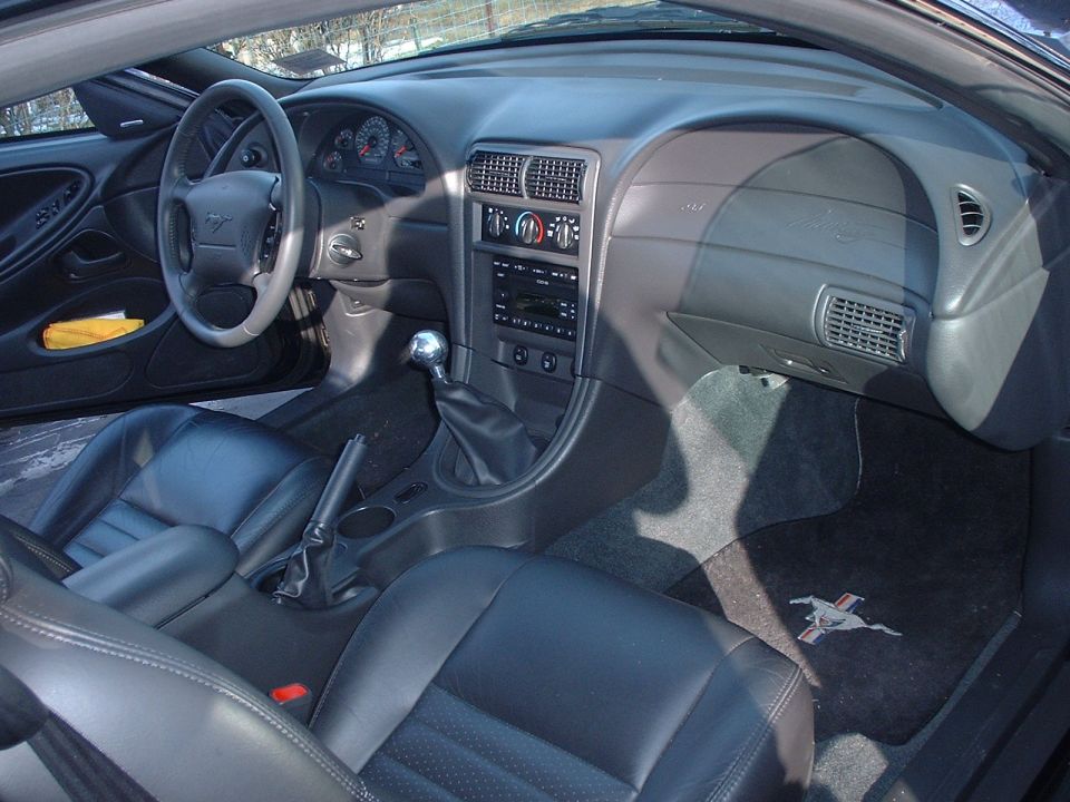 Interior shot of a 2002 Ford Mustang, showing black leather seats, dashboard, steering wheel, and gear shifter